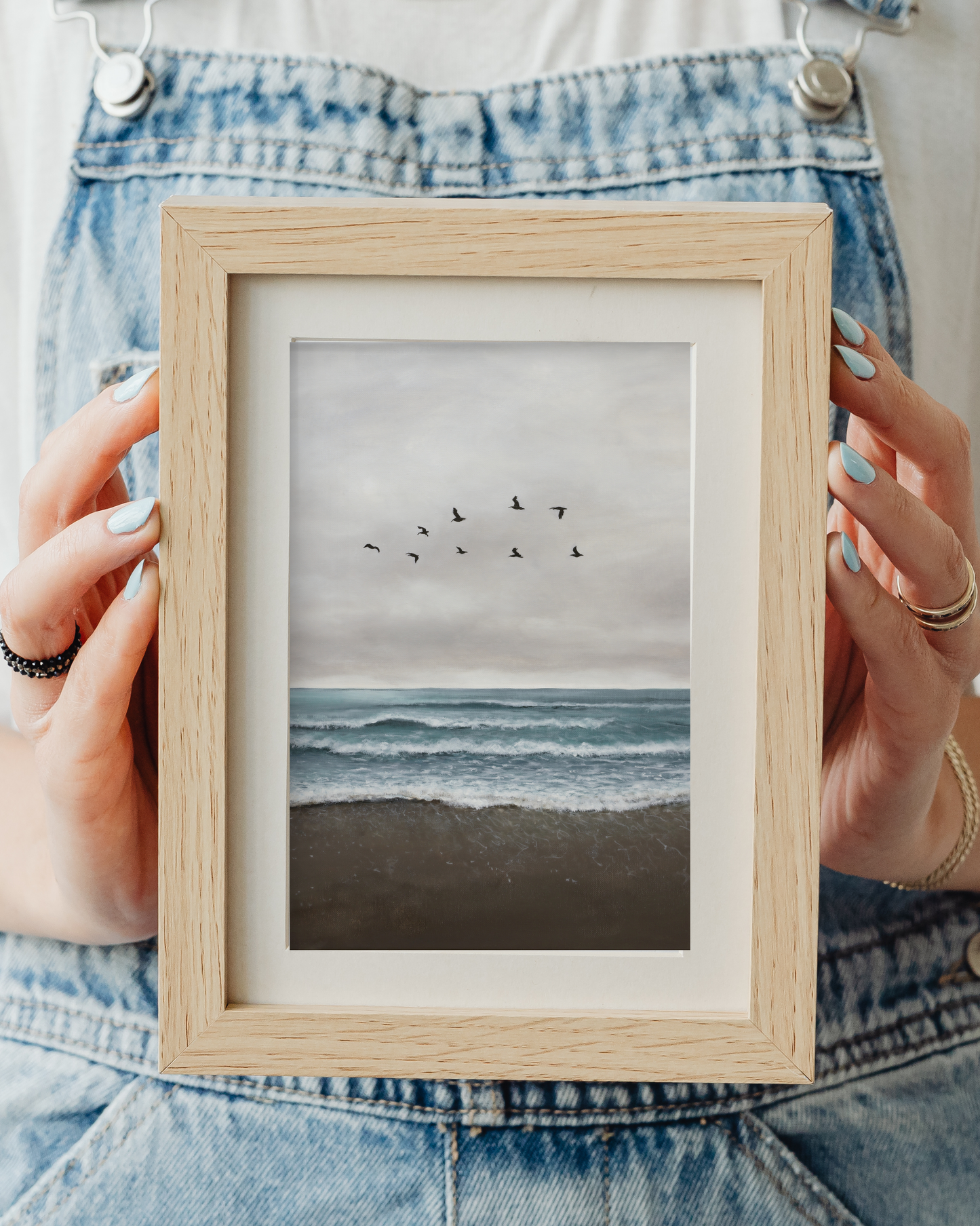 Person holding a framed artwork of a beach scene with birds.