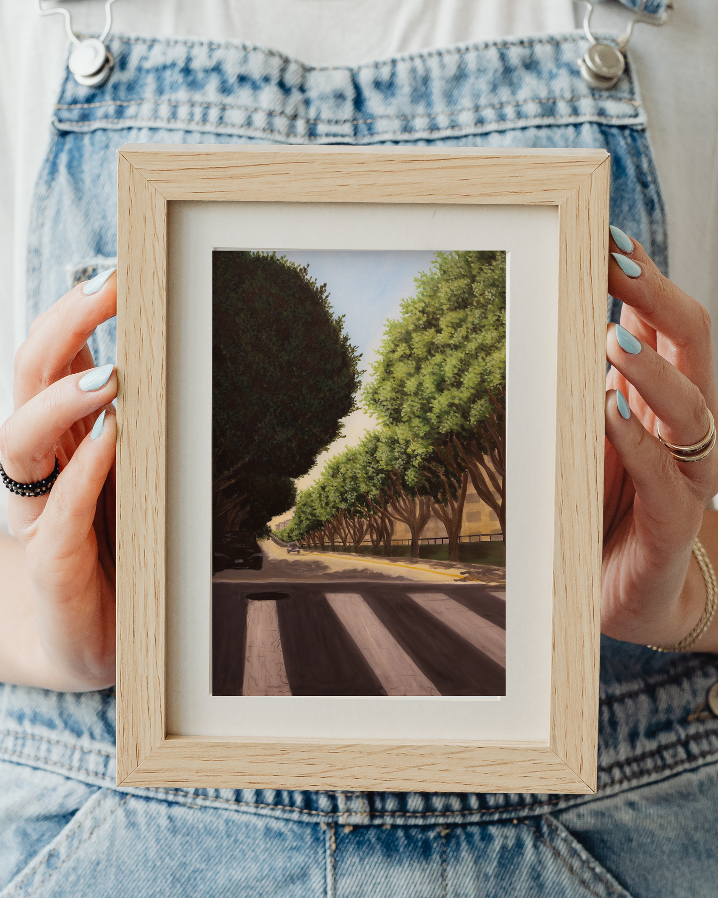 Person holding a framed photograph of a tree-lined road art print for sale